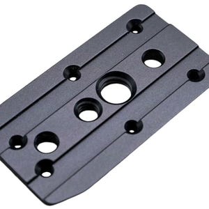 Puede incluir: Una placa metálica rectangular negra con múltiples orificios circulares y ranuras. La placa tiene un acabado mate y parece ser un componente de un dispositivo más grande. El diseño sugiere una placa de montaje o base.