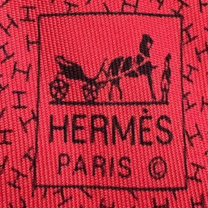 May include: Close-up of a red textile with a repeating pattern of black "H" shapes. The center features a black logo with a horse-drawn carriage and the words "HERMES PARIS ©".
