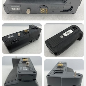 May include: Black camera battery grip with multiple ports and buttons. The grip has a textured surface and a label that reads "Olympus Power Lithium Battery Pack - Li-ion".