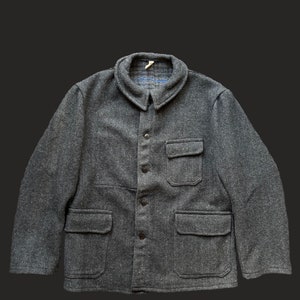 Op de afbeelding: Een grijze visgraatjas met een kraag en vier voorzakken. De jas heeft een knoopsluiting en een klassiek ontwerp. De stof lijkt een wolmix te zijn, geschikt voor koeler weer.