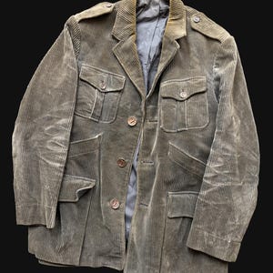 Op de afbeelding: Een vintage olijfgroene corduroy jas met vier voorzakken en knoopsluitingen. De jas heeft schouderstukken en een revers. De voering is een donkerdere tint groen. Klassieke stijl.