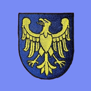 May include: A blue and yellow embroidered patch featuring a stylized eagle with outstretched wings. The eagle is centered on a blue shield with a black outline.