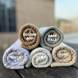 May include: Five rolled up fabric swatches in different shades of beige, white, and light blue. The swatches are labeled "Golden Rod", "Sage Pale", "White", "Ivory", and "Bone".