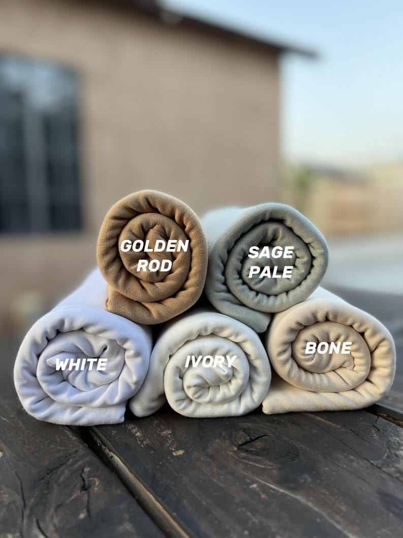 May include: Five rolled up fabric swatches in different shades of beige, white, and light blue. The swatches are labeled "Golden Rod", "Sage Pale", "White", "Ivory", and "Bone".