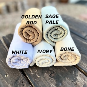 May include: Five rolled up fabric swatches in different shades of white, beige, and green. The swatches are labeled "White", "Ivory", "Bone", "Golden Rod", and "Sage Pale".