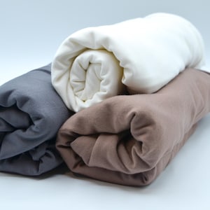 May include: Three rolled up fabric swatches in different colors: dark gray, brown, and white.