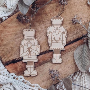 Könnte beinhalten: Zwei hölzerne Nussknacker-Anhänger, einer mit Bart und Hut, der andere mit Bart und Hut, beide mit einem detaillierten Design.