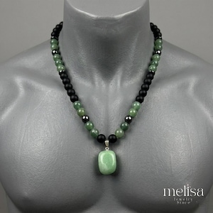 May include: A beaded necklace featuring alternating matte black beads, polished green stone beads, and small metallic dark grey spheres. A large, smooth, rectangular green stone pendant hangs from the center of the beaded strand.