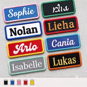 Op de afbeelding: Acht rechthoekige geborduurde naamlabels met gekleurde randen. De labels bevatten de namen Sophie, Nolan, Arlo, Isabelle, Klia, Lieha, Cania en Lukas in verschillende lettertypes en garenkleuren op blauwe, zwarte, rode en grijze achtergronden.