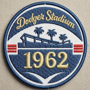 May include: Embroidered patch featuring "Dodger Stadium" in gold script above a stadium graphic with palm trees and the year "1962". The patch is circular with a blue and white design and red stripes.