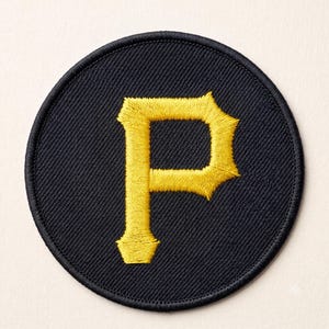 Op de afbeelding: Een ronde geborduurde patch met een zwarte achtergrond en een opvallende, gele letter P in het midden gestikt. De patch heeft een dikke, zwart gestikte rand die de ronde vorm definieert en zorgt voor een nette, afgewerkte rand.