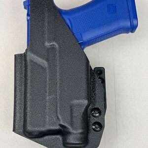 Puede incluir: Una funda de cuero negra para una pistola con una empu&ntilde;adura de pol&iacute;mero azul. La funda tiene un clip para cintur&oacute;n y varios tornillos.