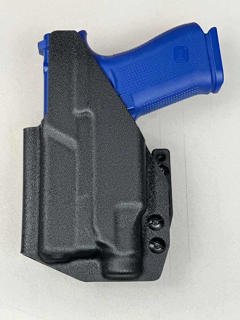 Puede incluir: Una funda de cuero negra para una pistola con una empu&ntilde;adura de pol&iacute;mero azul. La funda tiene un clip para cintur&oacute;n y varios tornillos.