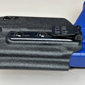 Puede incluir: Una funda negra con una superficie texturizada y un clip de metal negro con la palabra "ULTI-CLIP" impresa en &eacute;l.