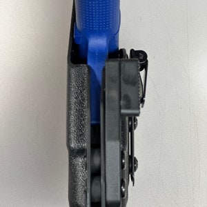 Puede incluir: Una funda de pol&iacute;mero negra con una pistola azul en su interior. La funda tiene un clip para cintur&oacute;n y retenci&oacute;n ajustable.