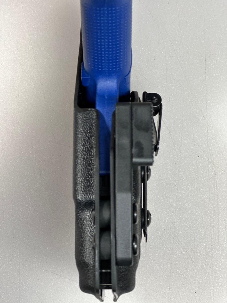 Puede incluir: Una funda de pol&iacute;mero negra con una pistola azul en su interior. La funda tiene un clip para cintur&oacute;n y retenci&oacute;n ajustable.