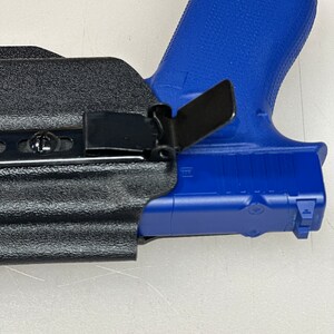 Puede incluir: Una funda de cuero negra con un clip de metal y una pistola de pl&aacute;stico azul en su interior.