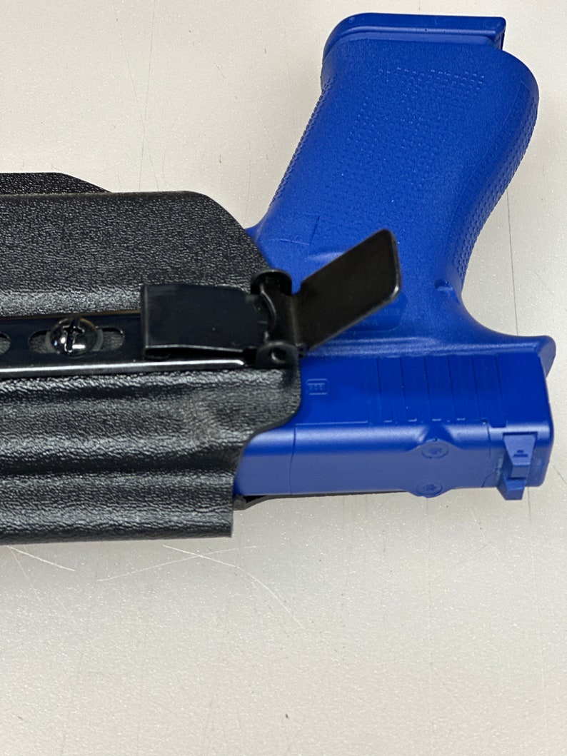 Puede incluir: Una funda de cuero negra con un clip de metal y una pistola de pl&aacute;stico azul en su interior.