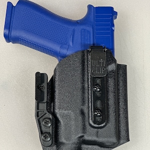 Puede incluir: Una funda de cuero negra con una pistola azul en su interior. La funda tiene un clip negro con el texto "ULTI CLIP" en &eacute;l.