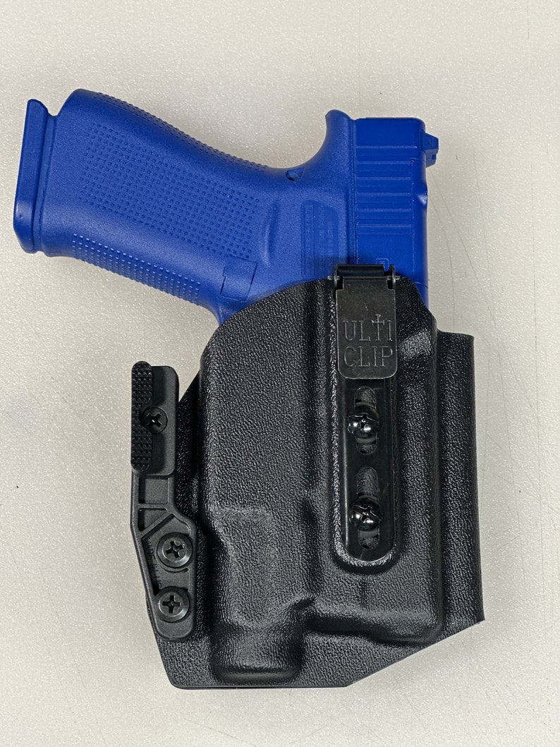Puede incluir: Una funda de cuero negra con una pistola azul en su interior. La funda tiene un clip negro con el texto "ULTI CLIP" en &eacute;l.