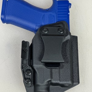 May include: A black polymer holster with a clip for carrying a blue handgun. The holster has a textured surface and multiple screws.