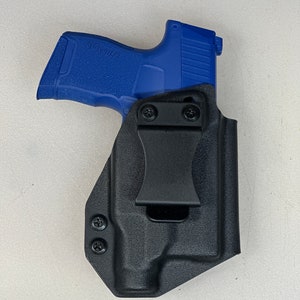 May include: A black leather holster with a clip for carrying a blue handgun. The handgun has the text "SIG SAUER" on the side.