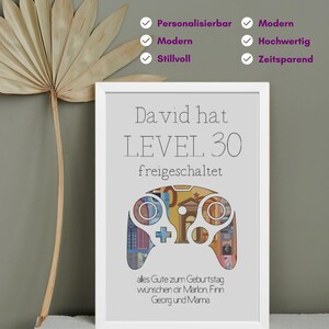 May include: A white framed print with a gray background. The print features a gray video game controller made of euro bills. The text "David hat LEVEL 30 freigeschaltet" is at the top of the print. The text "ales Gute zum Geburtstag w&uuml;nschen dir Marlon Finn Georg und Mama" is at the bottom of the print.