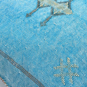 May include: A blue throw pillow with a white geometric pattern. The pillow has a brown border and is made of a woven fabric.