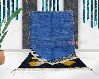 Puede incluir: Una alfombra marroquí azul y negra con patrones geométricos y acentos amarillos. La alfombra tiene un borde de flecos y está hecha de lana.