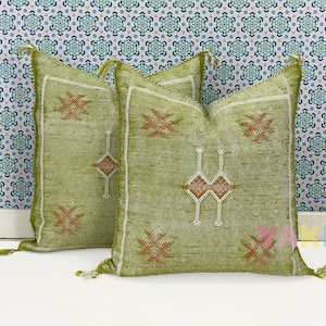 May include: Two green throw pillows with a geometric pattern and tassels. The pillows have a white background with brown and white embroidery.
