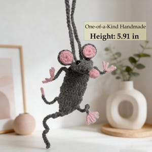 Könnte beinhalten: Handgefertigte graue Häkelratte mit rosa Ohren, Pfoten und Nase. Die Ratte wird an einem grauen Faden aufgehängt. Der Text "One-of-a-Kind Handmade" und "Höhe: 15 cm" sind sichtbar.