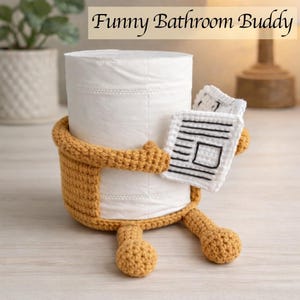 May include: A novelty toilet roll holder, hand-crocheted in yellow-brown, shaped like a character holding a small crocheted newspaper. The text "Funny Bathroom Buddy" is at the top. A fun bathroom accessory.