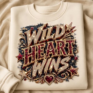 May include: A cream-colored crewneck sweatshirt featuring a central graphic with the text WILD HEART WINS. The lettering is rendered in a three-dimensional style with gold, diamond-like, and deep red gemstone textures, accented by stars and a heart.