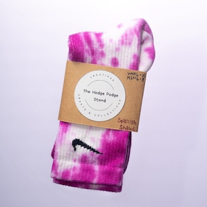 K&ouml;nnte beinhalten: Rosa-wei&szlig;e Batik-Socken mit einem schwarzen Nike-Swoosh-Logo. Die Socken sind gefaltet und haben ein braunes Etikett mit dem Text "CREATIONS The Hodge Podge Stand CRAFTS & COLLECTIONS WMNG-10 MENG-8 Spanish Shawl".