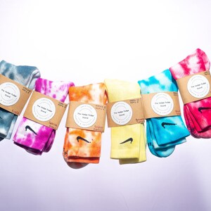 K&ouml;nnte beinhalten: Sechs Paar bunte Batik-Socken mit einem schwarzen Nike-Swoosh-Logo. Jedes Paar hat ein braunes Papieretikett mit dem Text "The Vintage Fudge Stand" in einem Kreis.