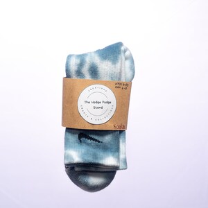 K&ouml;nnte beinhalten: Ein Paar blaue Batik-Socken mit einem schwarzen Nike-Swoosh-Logo. Die Socken sind gefaltet und mit einem braunen Etikett verpackt, auf dem "The Hodge Podge Stand, Crafts & Collections, Koala, WMN 6-10, MEN 6-8" steht.