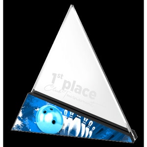 May include: A clear glass triangle trophy with a black base. The trophy has the words "1st place Club Tournament" engraved on it. The base has a blue and white abstract design with a bowling ball and pins.