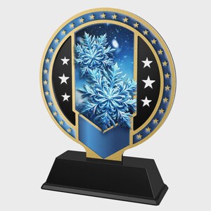 May include: A decorative trophy with a black base and a circular top. The top features a blue and gold design with snowflake imagery and white stars. The background is a snowy blue scene.