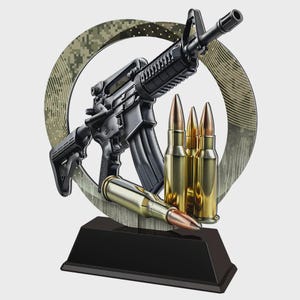 Puede incluir: Un rifle negro con cargador y balas, sobre un fondo circular con estampado de camuflaje. El rifle está montado sobre una base rectangular negra, creando una apariencia de trofeo.