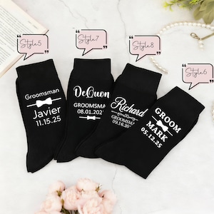 May include: Four black socks featuring white printed text and bow tie graphics. The socks display names such as Javier, DeQuon, Richard, and Mark, along with dates and titles like Groomsman and Groom. Each sock is labeled with a speech bubble style tag.