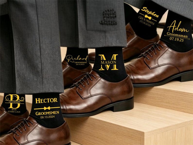 May include: Black socks with gold text and graphics, including names like Stephen, Adam, Richard, Mason, and Hector, along with the title Groomsman or Groomsmen, dates, and bow tie icons. The socks are worn with grey trousers and brown leather dress shoes.