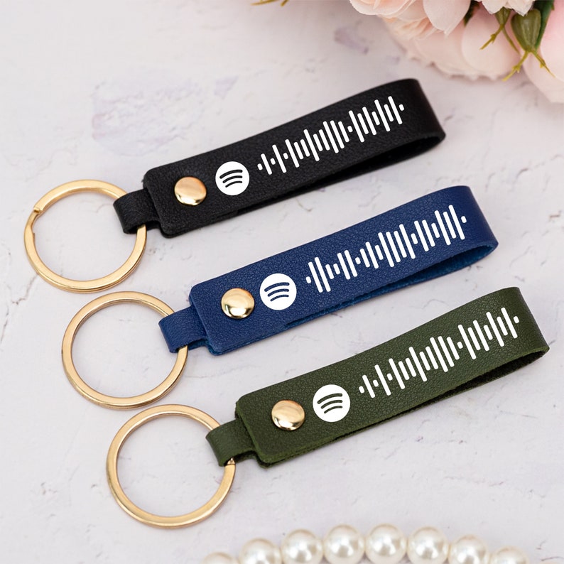 May include: Three leather keychains with gold key rings. Each keychain has a white Spotify logo and a white barcode printed on it. The keychains are black, blue, and green.