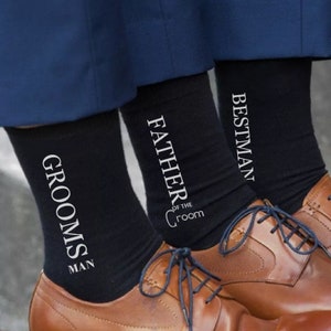 May include: Three pairs of black socks with white text. The socks say "Groom's Man", "Father of the Groom", and "Best Man".