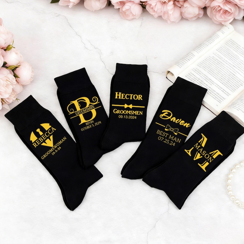 May include: Five black socks featuring gold printed text and graphics. The socks display names including Rebecca, Bryan, Hector, Davon, and Mason, along with titles like Groomswoman, Groomsman, and Best Man, plus specific dates and bow tie icons.