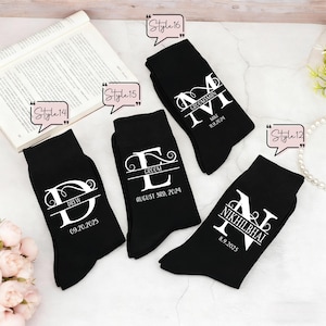 May include: Four black socks featuring white custom text and monograms. Each sock displays a large letter with a name and date printed underneath. The text includes DREW 09.20.2025, GROOM AUGUST 3RD, 2024, MIKE 11.9.2024, and NIKHILBHAI 8.9.2025, with style labels.