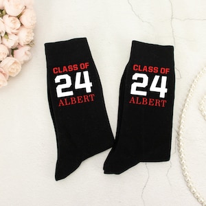 May include: Pair of black socks with white text that reads "Class of 24 Albert".