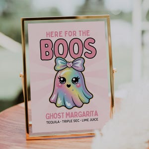 Könnte beinhalten: Ein gerahmtes Schild mit goldenem Rand zeigt einen niedlichen Cartoon-Geist mit einem Regenbogenkörper und einer Schleife. Auf dem Schild steht "HERE FOR THE BOOS" und "GHOST MARGARITA" mit den unten aufgeführten Zutaten.