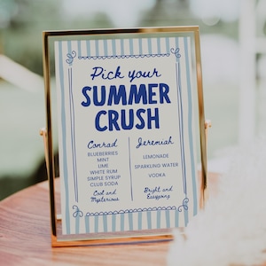 Puede incluir: Un letrero enmarcado con el texto "Pick your SUMMER CRUSH" en azul. Enumera recetas de cócteles para "Conrad" y "Jeremiah". El marco dorado descansa sobre una superficie de madera.