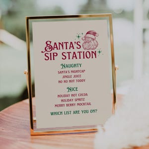 May include: A framed sign with gold trim displays "Santa's Sip Station" in burgundy script, with a Santa illustration. The sign lists "Naughty" and "Nice" drink options for the holidays, including "Holiday Hot Cocoa" and "Jingle Juice".
