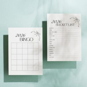 May include: Two white paper sheets with the text "2026 BINGO" and "2026 BUCKET LIST" in black script. Each sheet has a decorative bow illustration. The bingo card has a grid, and the bucket list has a list of goals.